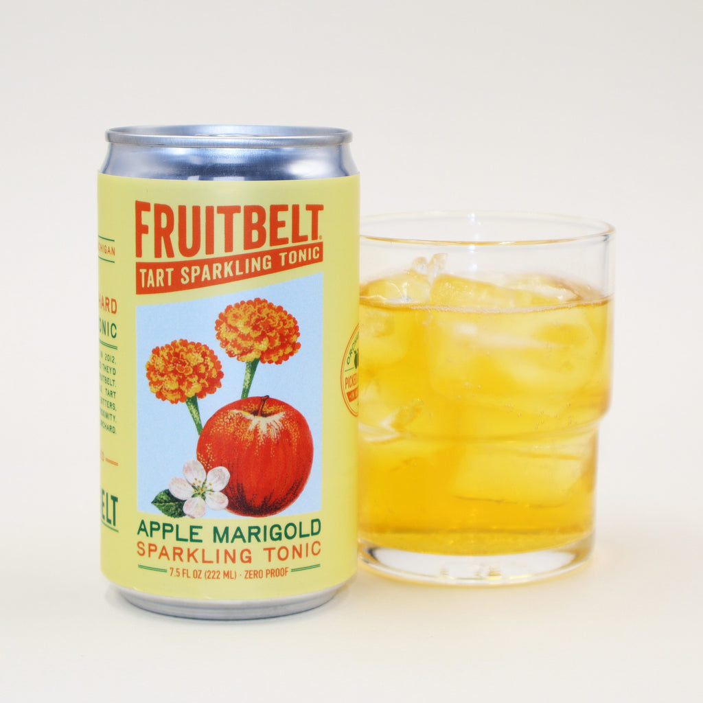 A can of Fruitbelt Tart Sparkling Tonic in Apple Marigold flavor stands next to a clear glass filled with an amber-colored drink and ice cubes on a clean white background.