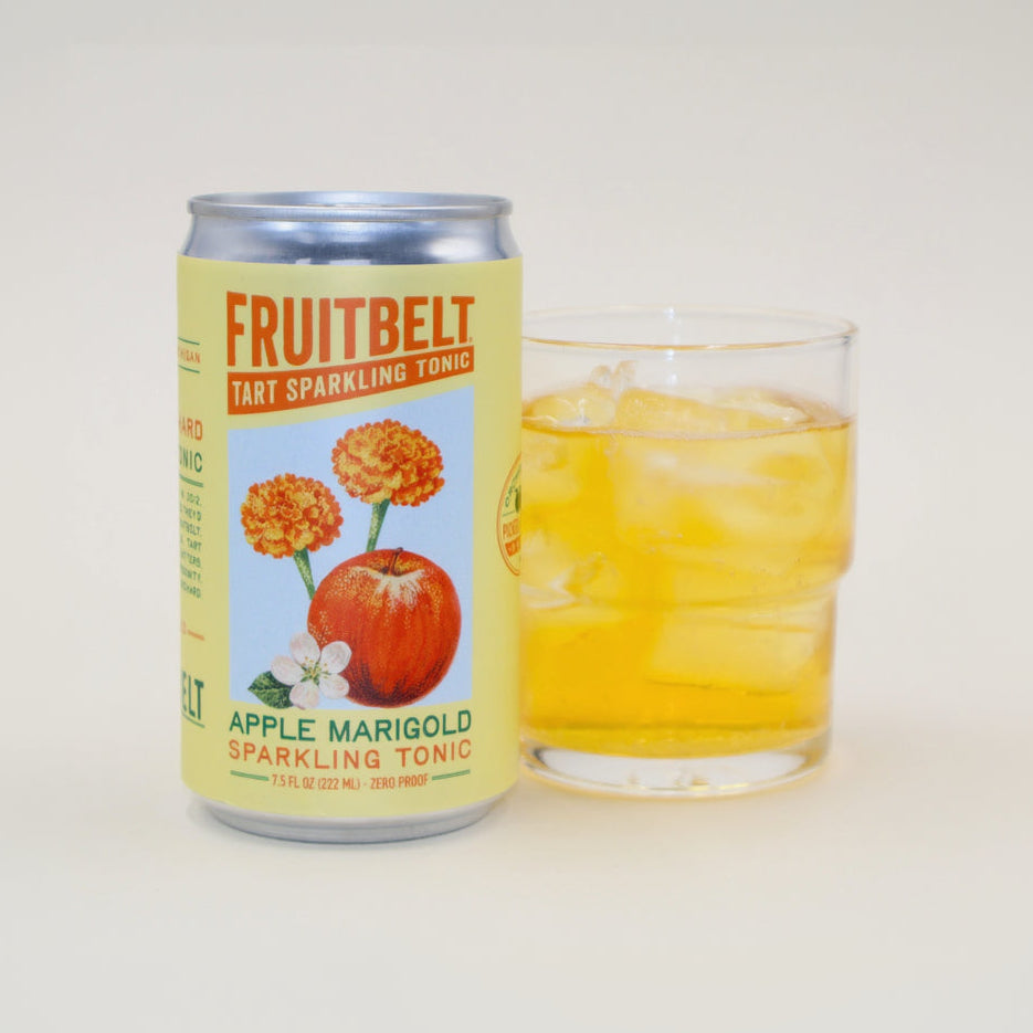 A can of Fruitbelt Tart Sparkling Tonic in Apple Marigold flavor stands next to a clear glass filled with an amber-colored drink and ice, on a plain light background.